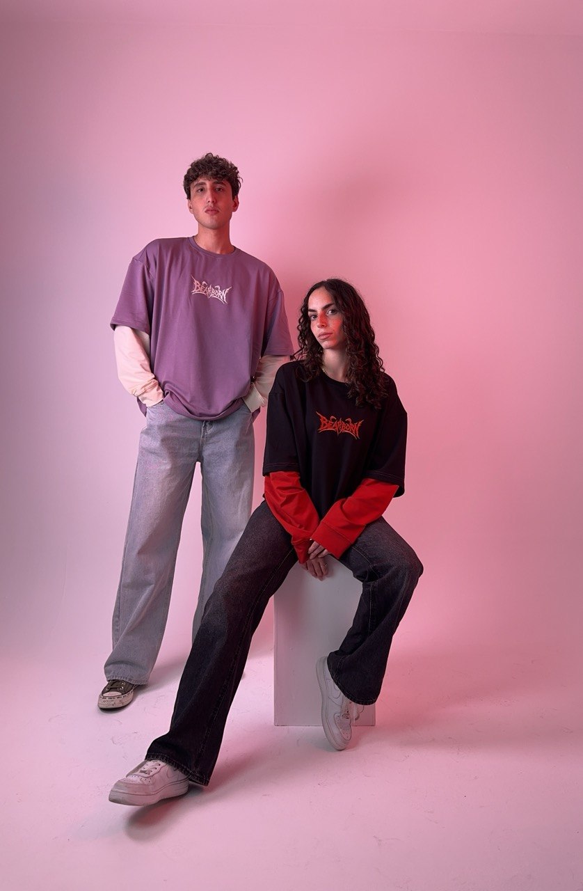 Two models wearing the Y2K Double Layer Tee — purple with bone sleeves and black with red sleeves — in a pink studio